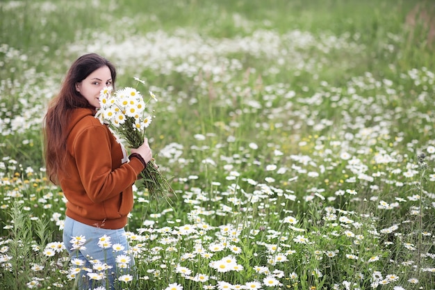Beautiful girl collects daisies in summer day in afield