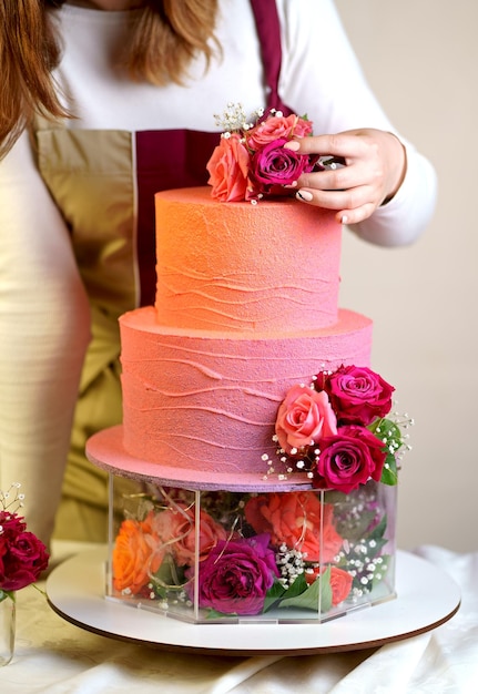 Beautiful girl confectioner in a working apron decorates a birthday cake with fresh flowers