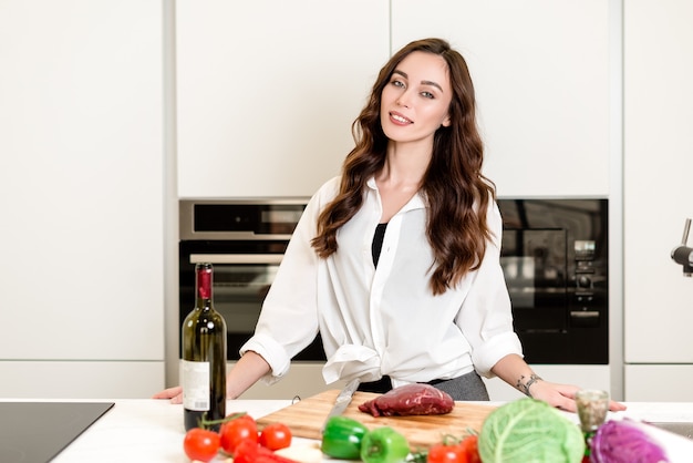 Beautiful girl cooking meat at the kitchen with vegetables