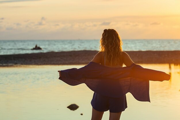 海岸の夕日の光の中で美しい少女が踊り、回転する