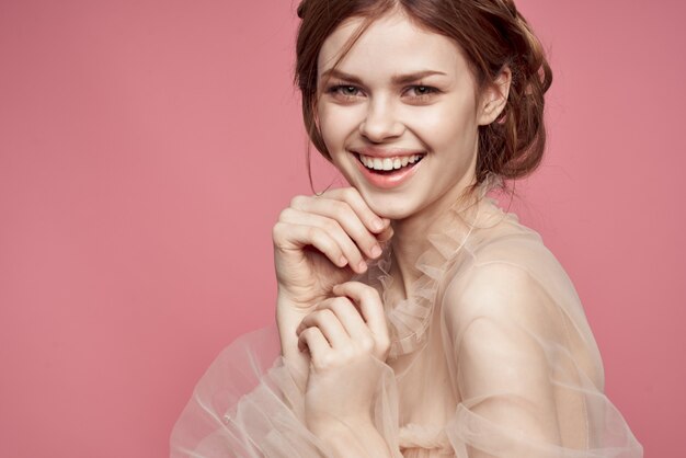 Beautiful girl in a delicate dress smiles on a pink background