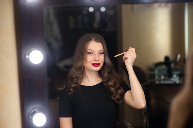 La bella ragazza fa il trucco e si guarda allo specchio