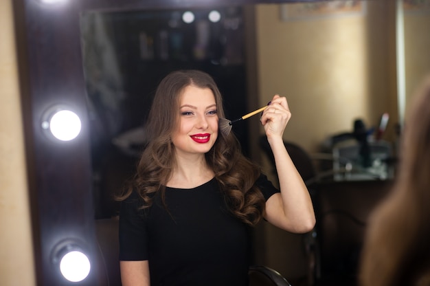 La bella ragazza fa il trucco e si guarda allo specchio