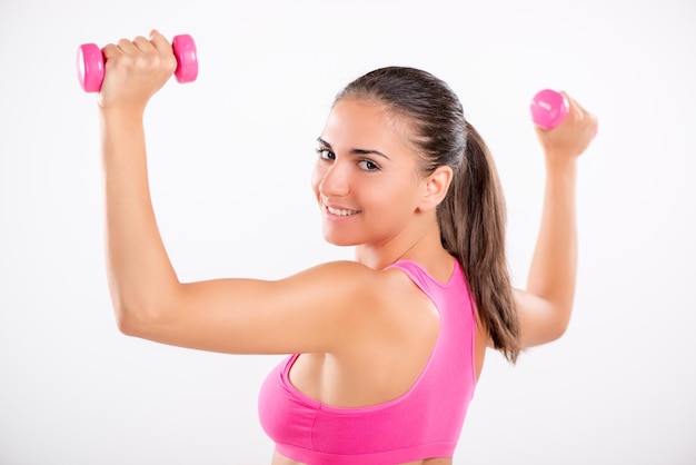 Beautiful girl doing exercise to strengthen shoulder with dumbbell. Looking at camera. White background.