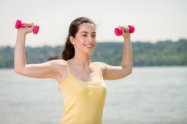 Beautiful girl doing exercise with dumbbell by the river.