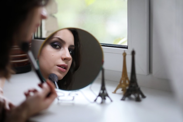 Beautiful girl doing makeup in front of a mirror