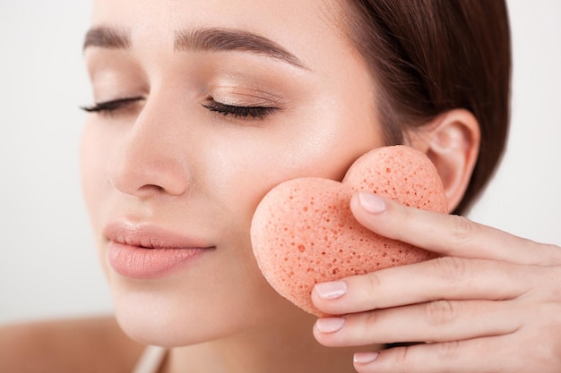 Beautiful girl doing makeup with a heartshaped sponge