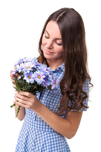 흰색 배경에 손에 국화 꽃이 있는 파란색 새장에 드레스를 입은 아름다운 소녀