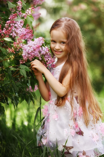 Beautiful Girl in dress posing near Bush of lilacs