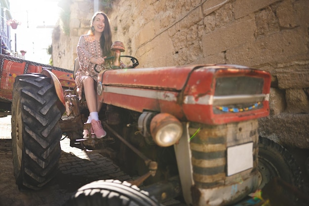 A beautiful girl in a dress rides an old tractor