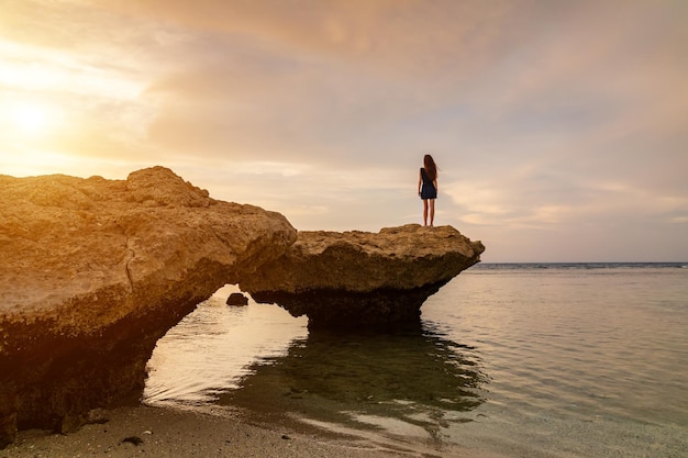 Beautiful girl in dress on the rocky beach at sunset Red sea