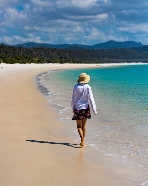 beautiful girl in dress and shirt and hat walks on whitehaven beach, whitsunday island, australia