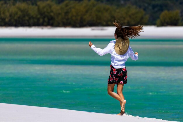 a beautiful girl in a dress, shirt and hat walks on the whitehaven beach, whitsundays