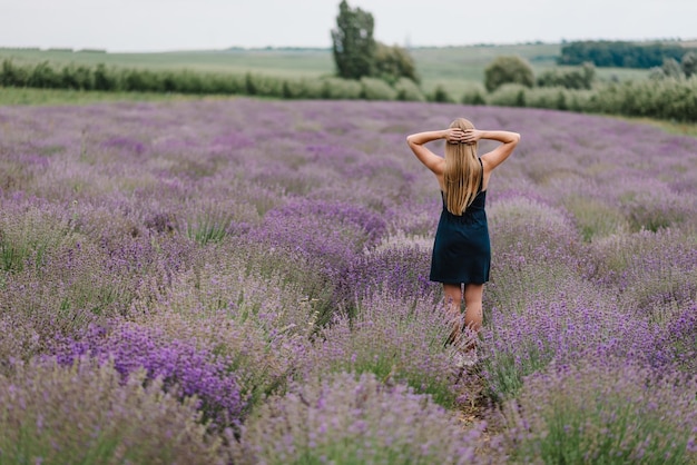 Bella ragazza in abito stand su viola il campo di lavanda bella donna cammina e guarda sul campo di lavanda al tramonto in francia soft focus godetevi la natura estiva della radura floreale vista posteriore