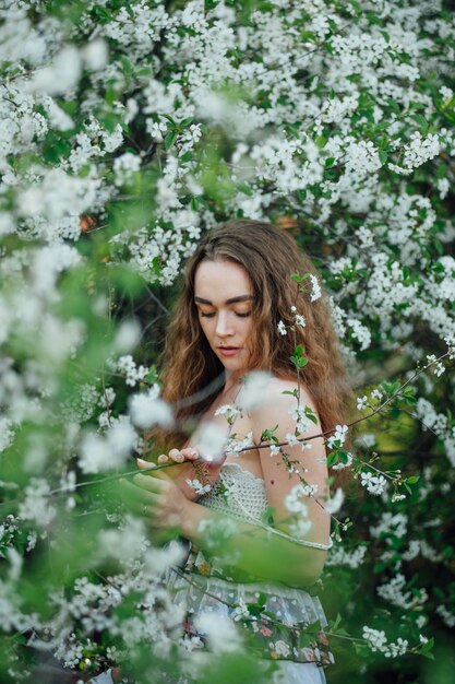 A beautiful girl in a dress stands next to a blooming cherry bus