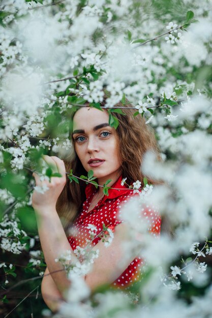 A beautiful girl in a dress stands next to a blooming cherry bus