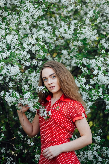 A beautiful girl in a dress stands next to a blooming cherry bus