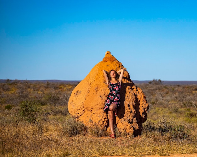 A beautiful girl in a dress stands by a huge termite mound in the desert in western australia