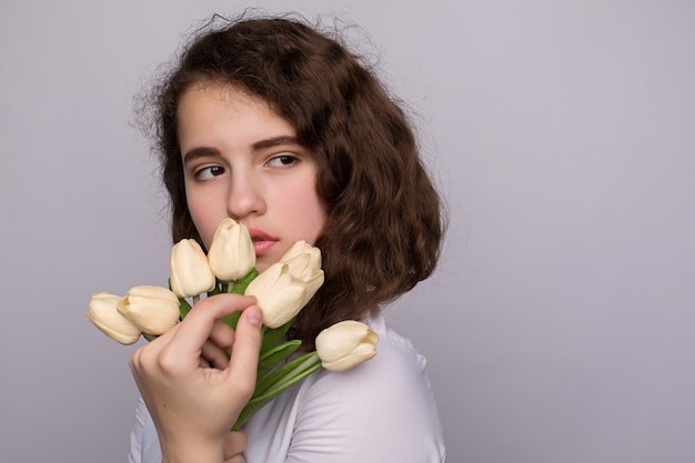 Bella ragazza in abito con fiori tulipani nelle mani su uno sfondo chiaro