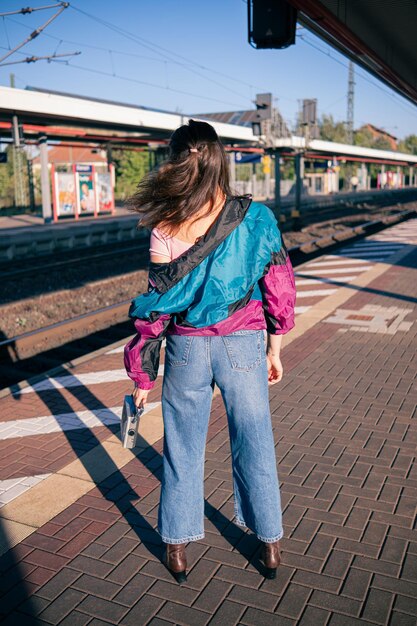 Beautiful girl dressed in 90s style with portable radio receiver in her hands posing on the platform of the train station