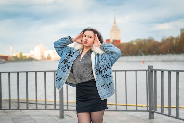 Una bella ragazza vestita con una giacca di jeans cammina lungo il molo sulle rive del fiume