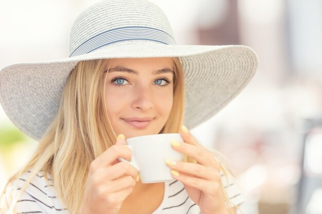 Beautiful girl drinking coffee in a cafe terrace. Summer portrait young woman.