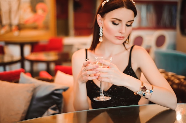 A beautiful girl drinks martini in the hotel lobby and is waiting for her young boyfriend