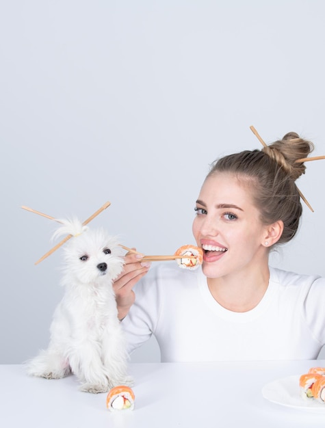 Beautiful girl eating japanese sushi rolls with chopsticks funny dog order in fastfood restaurant Beauty woman with pet puppy holding sushi with chopsticks