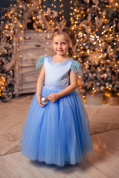 Beautiful girl in an elegant dress against the background of Christmas lights and a Christmas tree in a beautiful interior