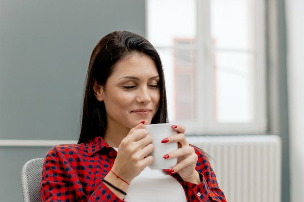 オフィスで最初の朝のコーヒーを楽しんでいる美しい少女。