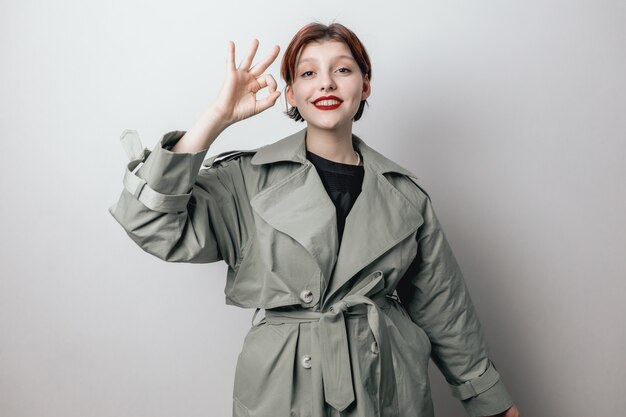 A beautiful girl in a fashionable green coat shows OK sign