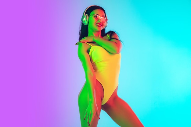 Beautiful girl in fashionable swimsuit isolated on gradient studio background in neon light.