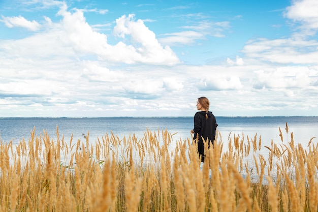 Beautiful girl in a field on the shore of the sea and blue sky with clouds