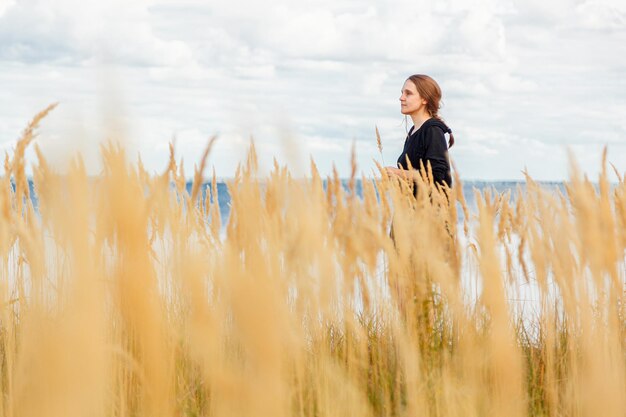 Beautiful girl in a field on the shore of the sea and blue sky with clouds