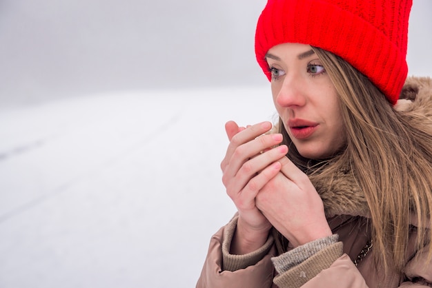 beautiful girl freezing in winter park. Girl warms her hands by breath. young beautiful brunette girl warms his hands in the cold