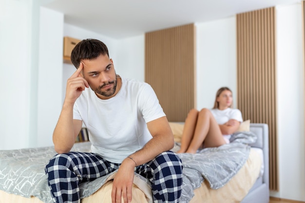 Beautiful girl and a frustrated man sitting in bed and not looking at each other Upset couple ignoring each other Worried man in tension at bed Young couple angry with each other after a fight