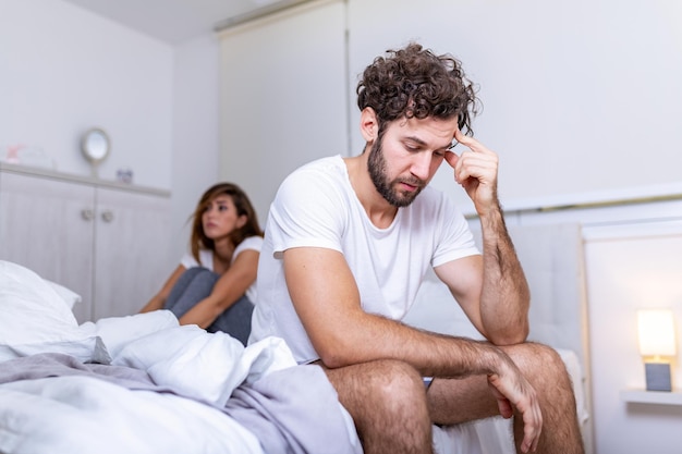 Beautiful girl and a frustrated man sitting in bed and not looking at each other. Upset couple ignoring each other. Worried man in tension at bed. Young couple angry with each other after a fight.