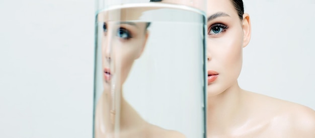 Beautiful girl under glass bottle with water clean skin young woman