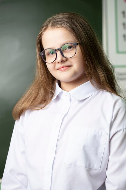 Beautiful girl in glasses of middle school age on the background of the blackboard