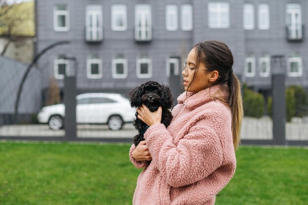 眼鏡とピンクのコートを着た美しい少女が建物の背景の芝生の上に立っています