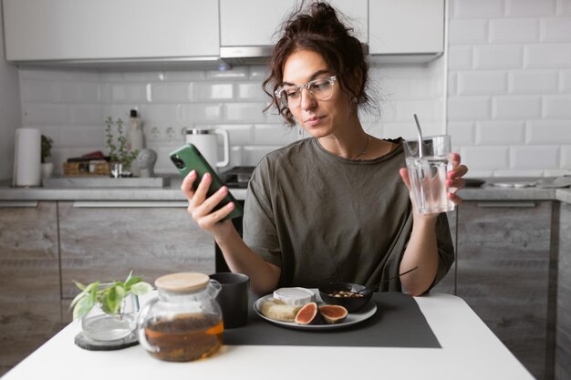 beautiful girl in glasses with curly hair and using phone eating morning snacks