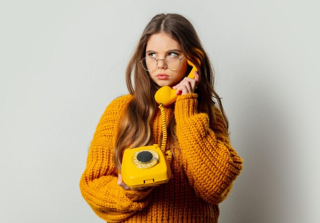 Beautiful girl in glasses and yellow sweater with yellow dial phone on white background