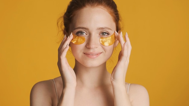 Beautiful girl in gold eye patches dreamily looking in camera over colorful background Beauty concept