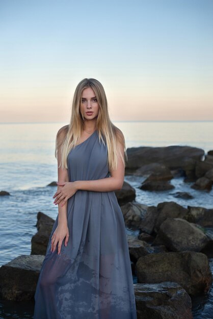 beautiful girl in a gray dress by the sea at sunset