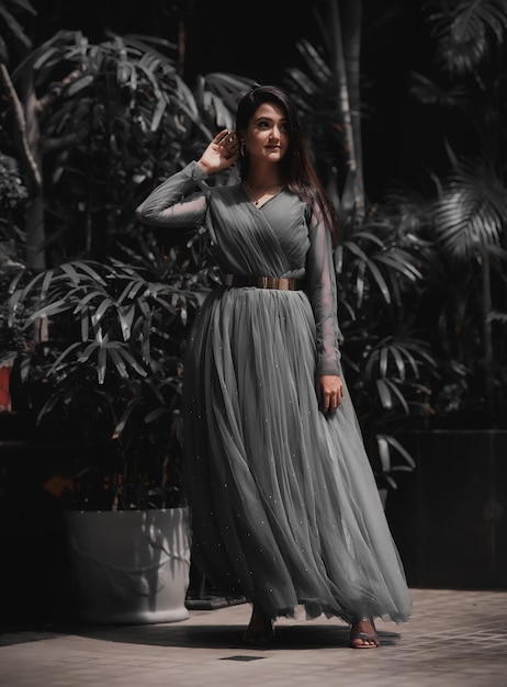 A beautiful girl in a gray gown dress posing in front of a palm tree