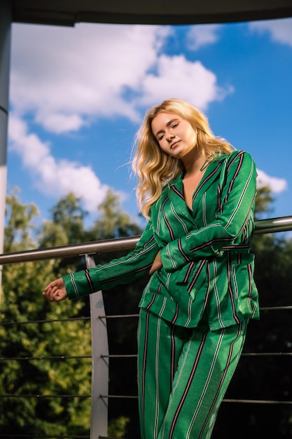 Photo beautiful girl in a green suit on a blurred city background stylish blonde fashionable girl