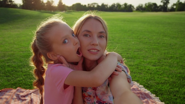 Beautiful girl grimacing with woman in city park Family taking selfie outdoor