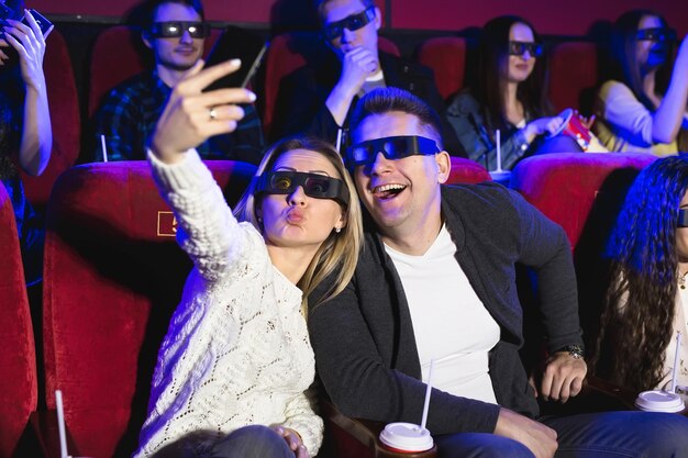 Bella ragazza e ragazzo che ridono felicemente facendo un selfie insieme durante un film al cinema