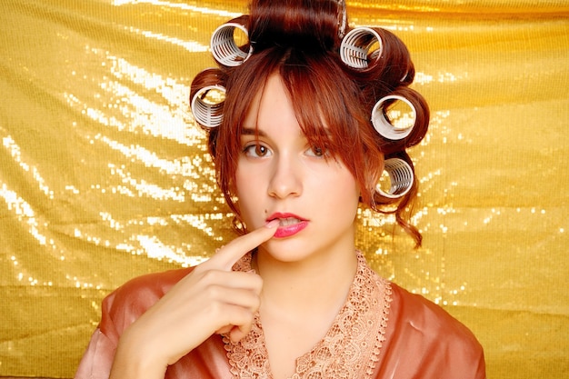 Beautiful girl in hair curlers isolated on golden background