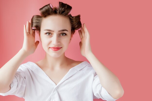 Beautiful girl in hair curlers on pink background.